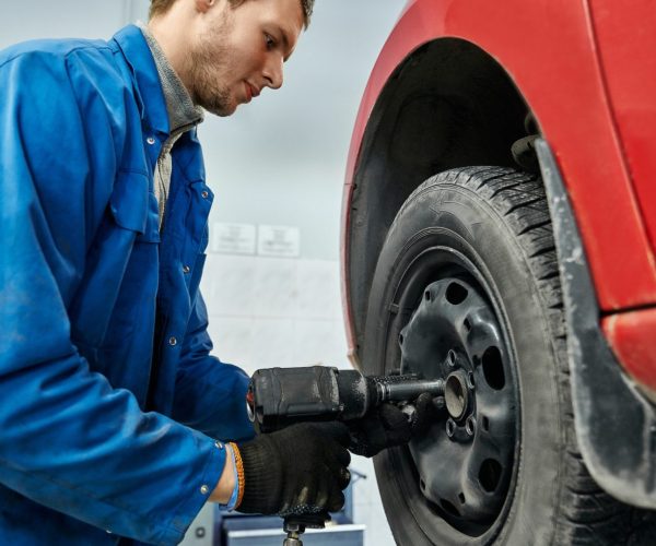 Auto mechanic changing car wheel with electric screwdriver